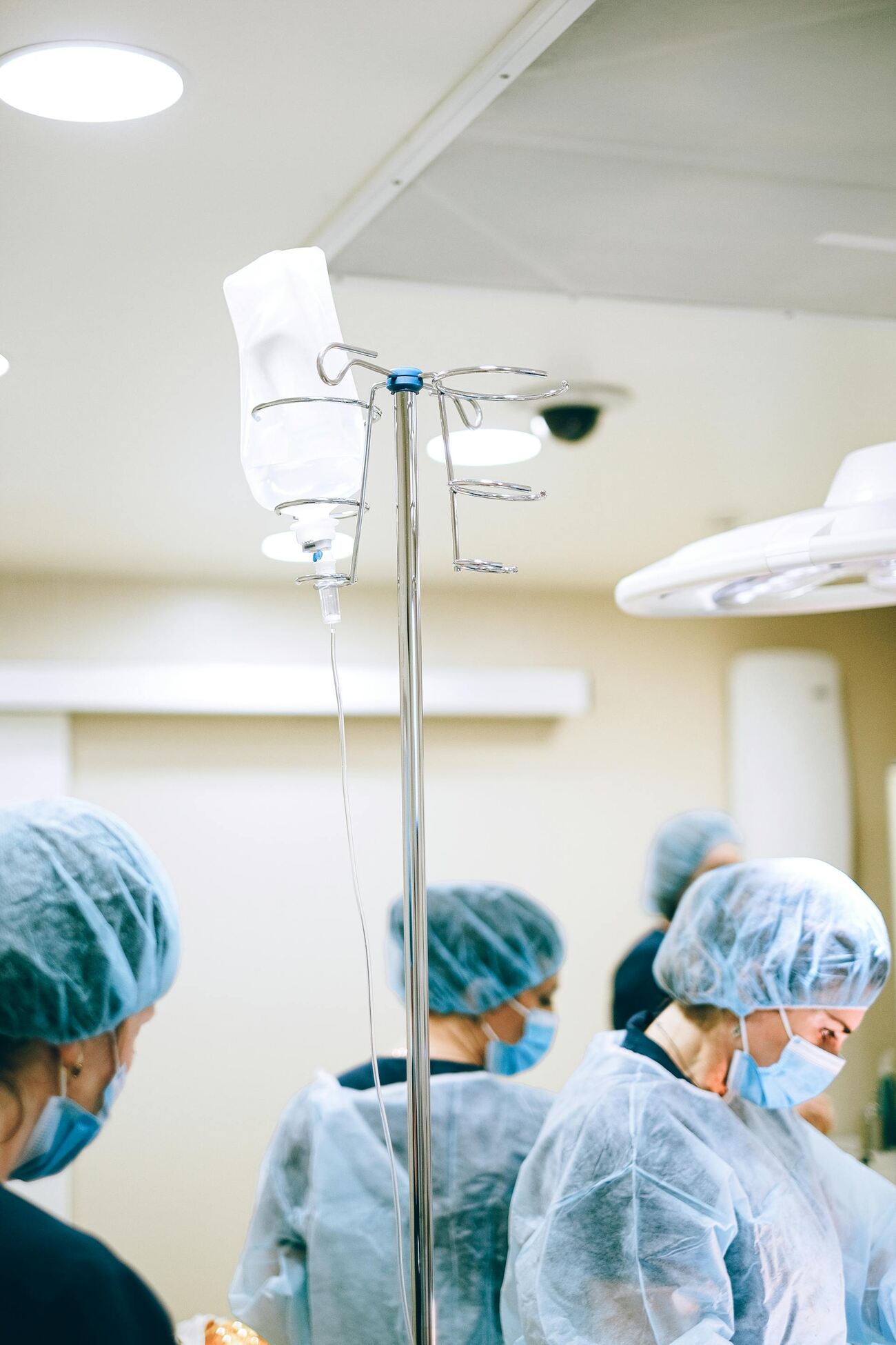 A close-up of an IV stand with medical staff in the background wearing protective gear