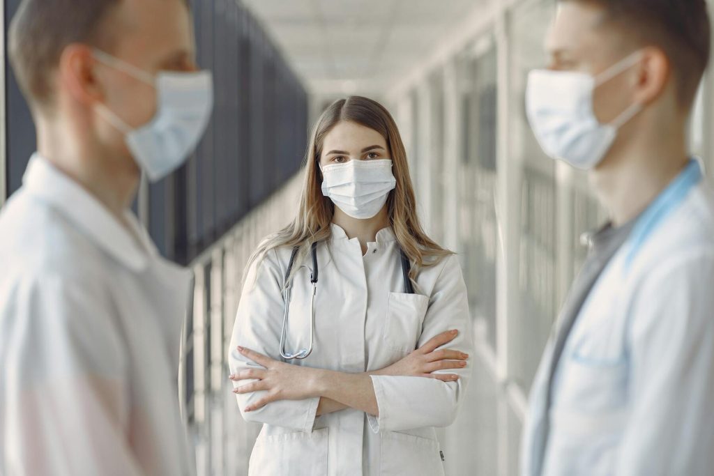 Three medical professionals in face masks standing in a hospital hallway