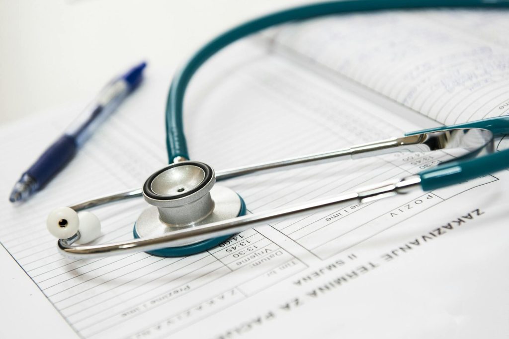 A stethoscope rests on top of medical paperwork and a pen