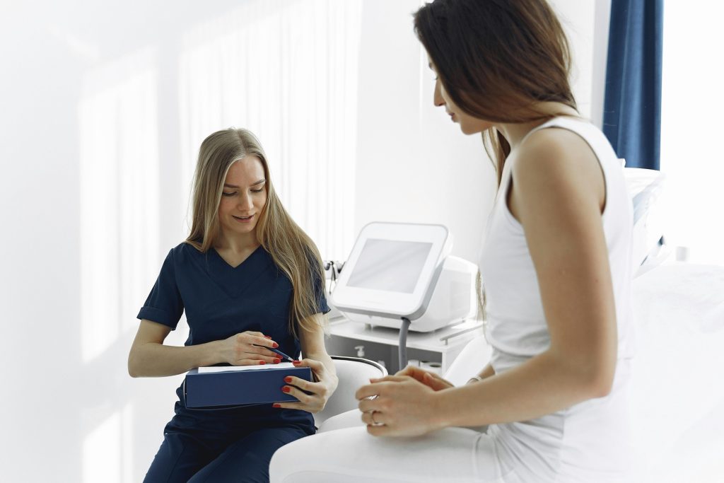 A nurse or medical professional in navy blue scrubs is interacting with a patient dressed in white