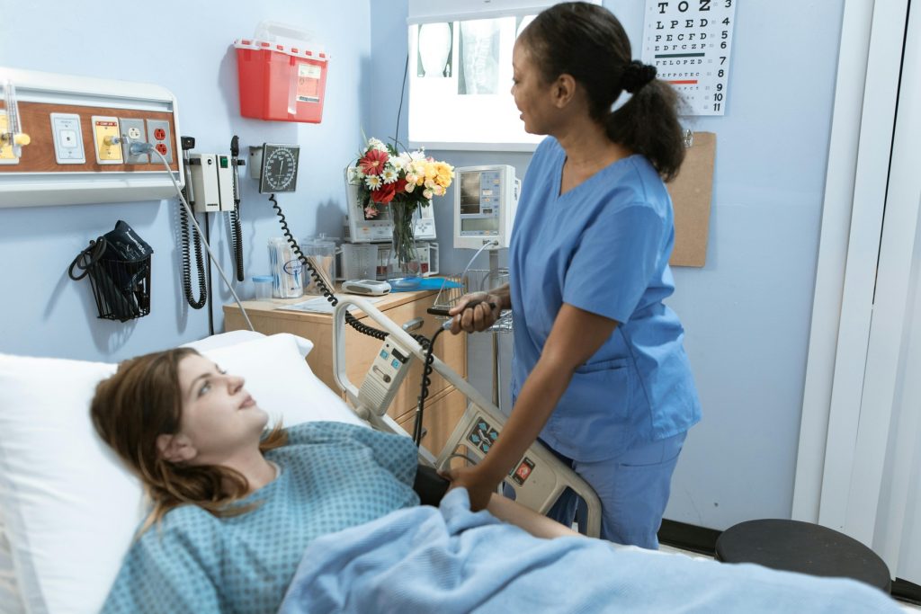 A nurse in blue scrubs is attending to a patient lying in bed