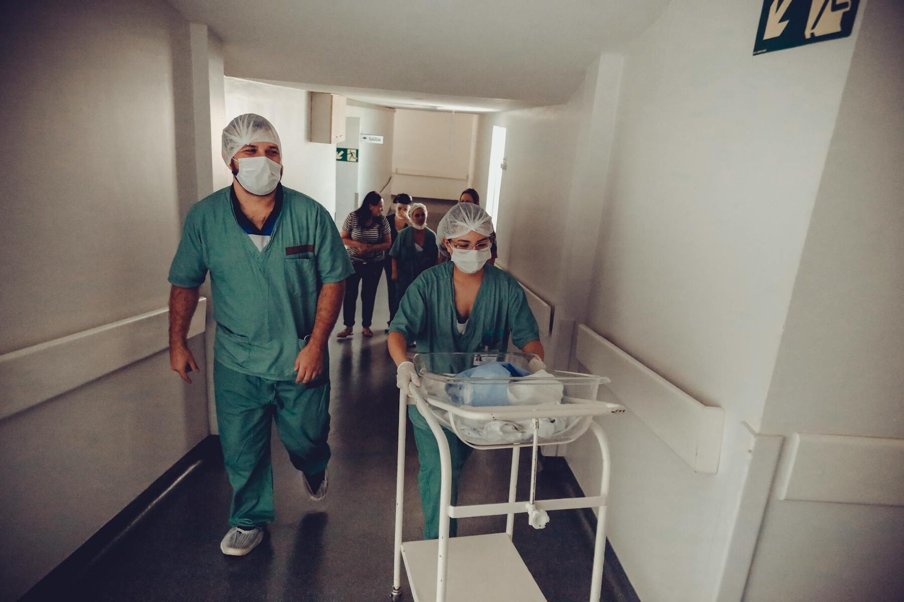 Medical staff walking down a hospital hallway with a newborn cart