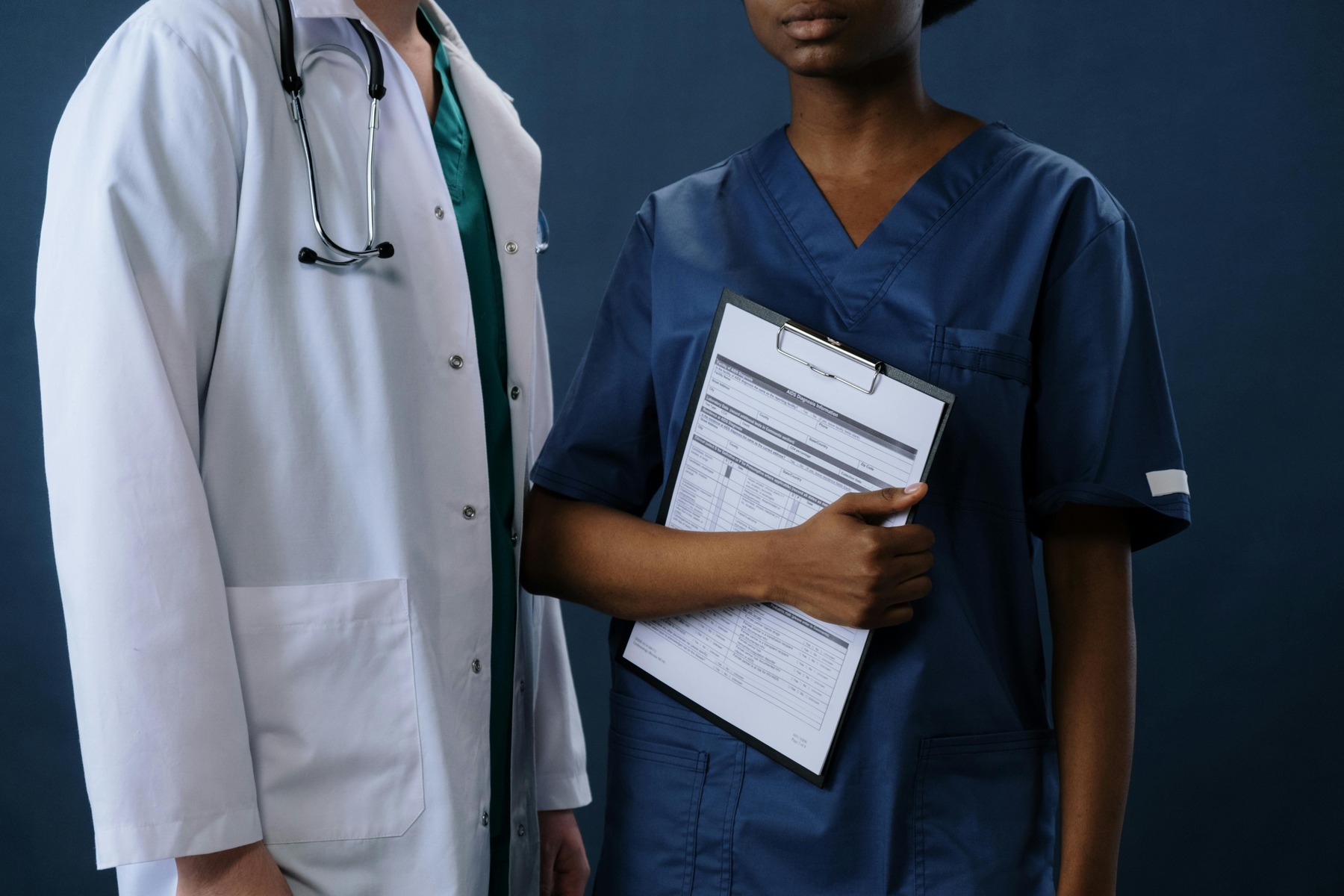 Two healthcare staff standing, one with white coat and the other a nurse holding nursing notes