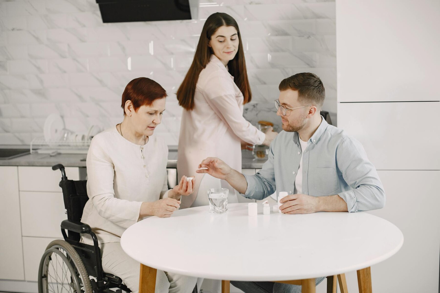 An elder woman in a wheelchair is seated at a table, engaged in conversation with a man and a woman beside her