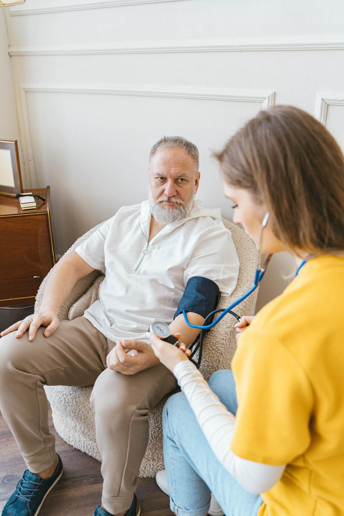 A nurse takes a blood pressure reading from an elderly patient sitting on a chair