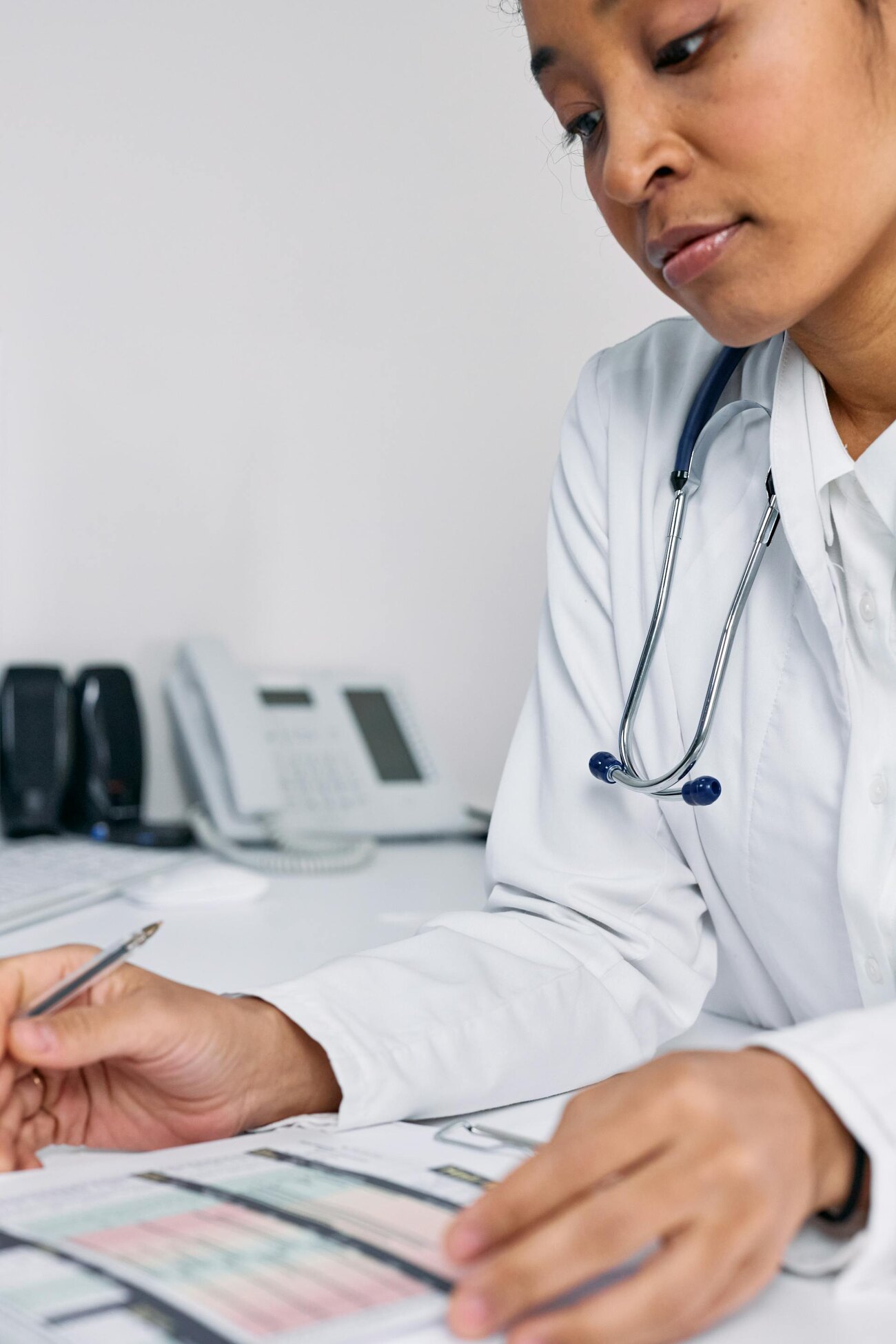 A doctor sitting at a desk, reviewing medical documents and writing with a pen