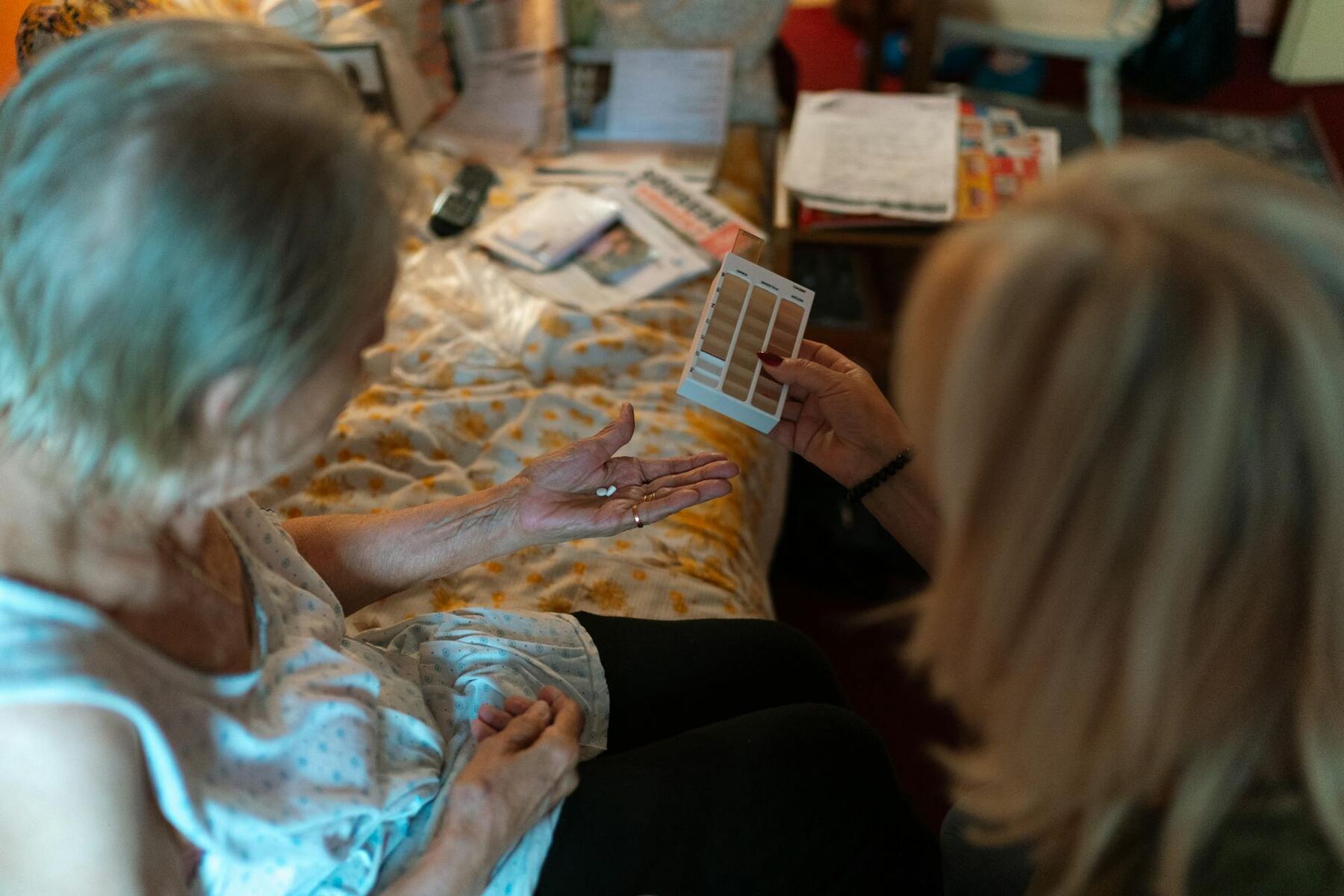 A caregiver showing a pill bottle to an elderly person in a bedroom